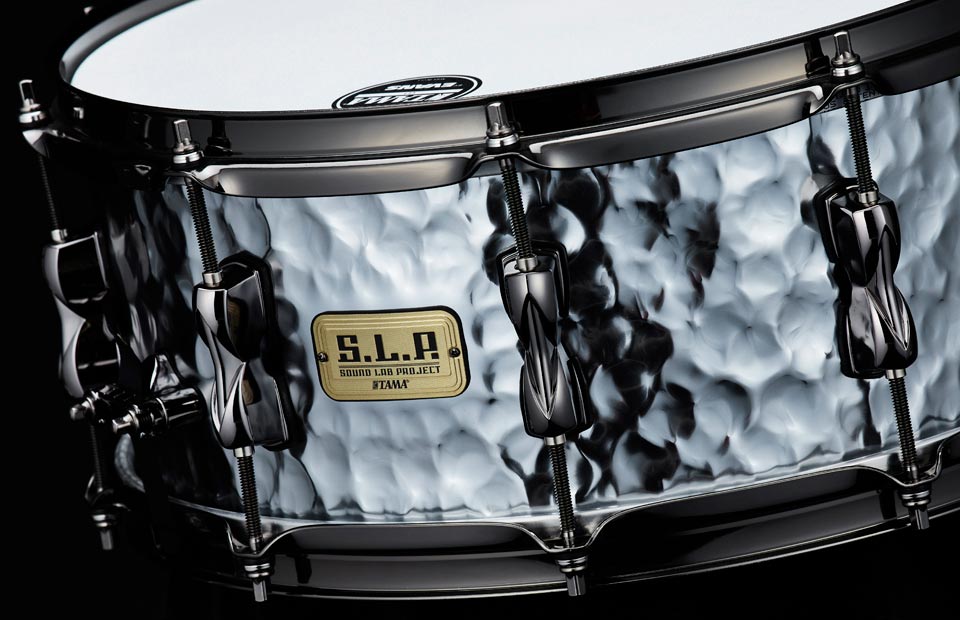 This TAMA S.L.P. Expressive Hammered Steel snare drum features a 14"x6" 1.2mm hammered steel shell. The Shallow depth hammering, glossy finish, and black nickel hardware deliver tonal complexity and sophisticated look. Outfitted with 2.3mm triple flange hoops and Starclassic Carbon Steel snare wires, this snare drum offers a crisp, dry attack with sensitive articulation to perfectly complement the naturally bright and clear steel shell. All of these features come together to create a uniquely musical and balanced snare drum, capable of being a workhorse snare in a wide variety of music styles.